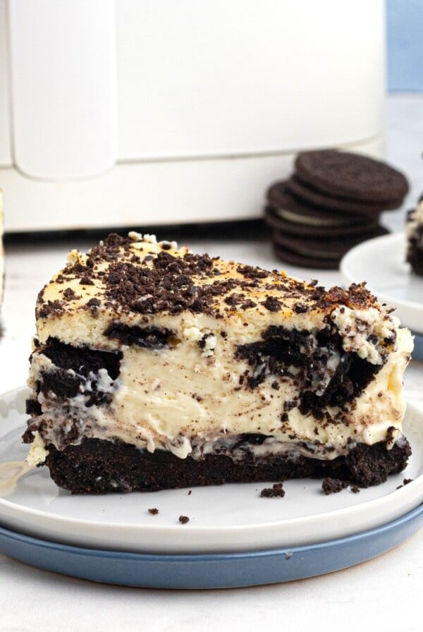 creamy slice of Oreo cheesecake served on a white plate in front of an air fryer.