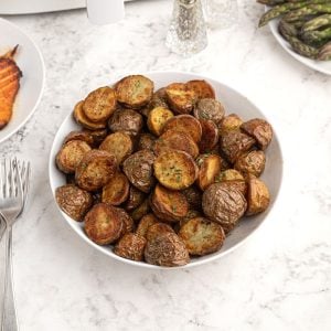 Roasted potatoes in a white bowl. Cooked and cut in half, topped with seasonings.