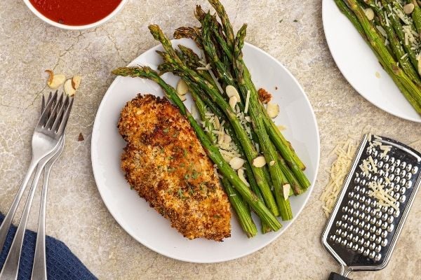 Parmesan Crusted Chicken on a white plate with cooked asparagus.