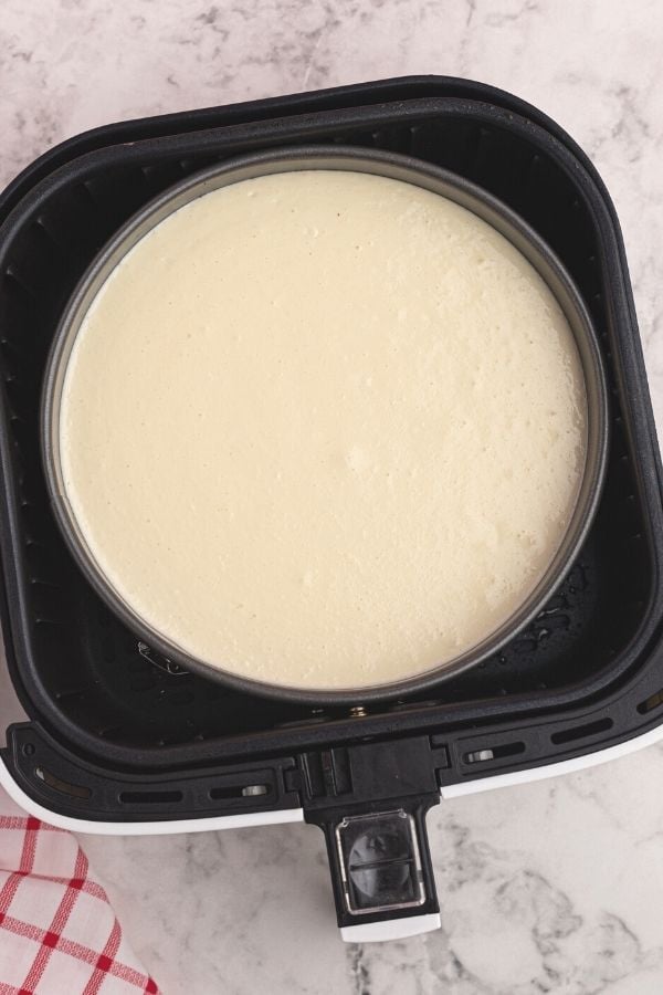 Uncooked cheesecake in a pan, placed inside the basket of an air fryer. 
