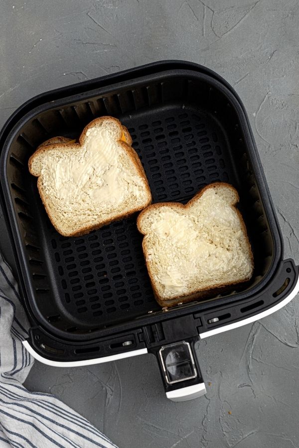 Uncooked bread in the air fryer basket with butter and cheese in the middle.