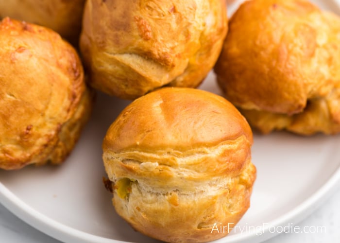 Close up of a batch of biscuit bombs on a white plate that are made with biscuit, egg, cheese, and bacon, and cooked in an Air Fryer. 