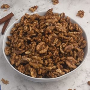 Candied Walnuts, served in a white bowl with cinnamon sticks and scattered walnuts on the table