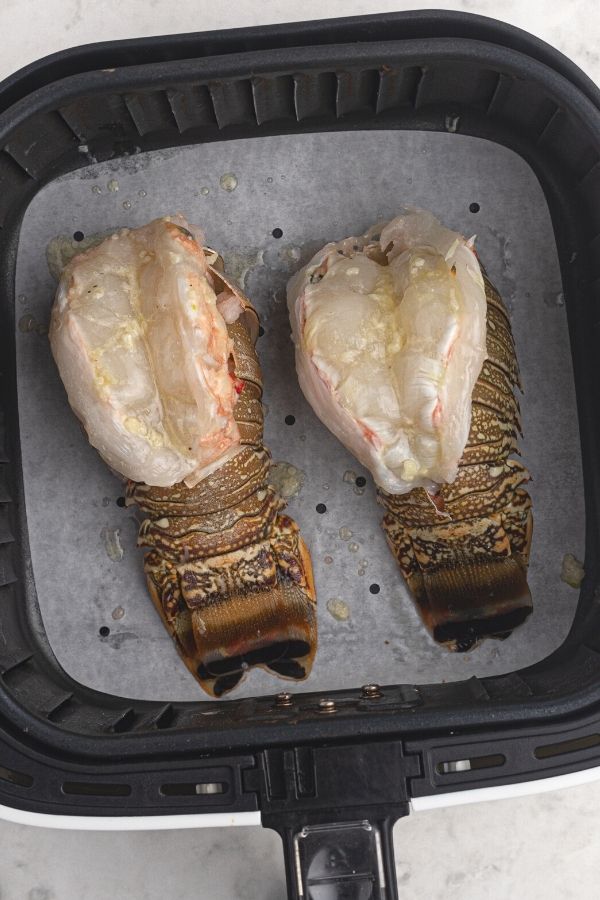 Uncooked lobster tails in the air fryer, sliced and brushed with butter and garlic. 