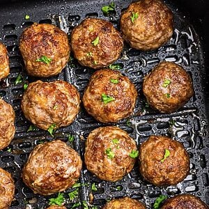 Golden brown juicy meatballs in the air fryer basket after being cooked.