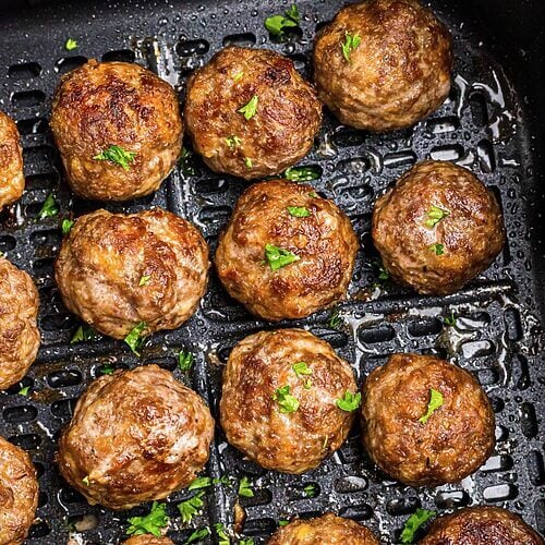 Golden brown juicy meatballs in the air fryer basket after being cooked.