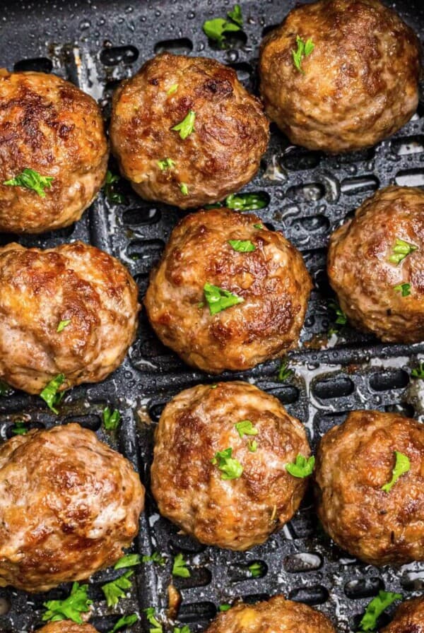 Golden brown juicy meatballs in the air fryer basket after being cooked.