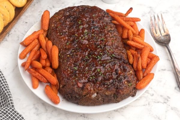 Air Fryer Meatloaf on a white plate with baby carrots around the meatloaf.