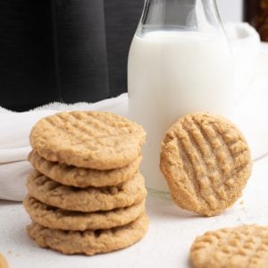 A stack of peanut butter cookies made in the Air Fryer with a glass of milk and the Air Fryer in the background.