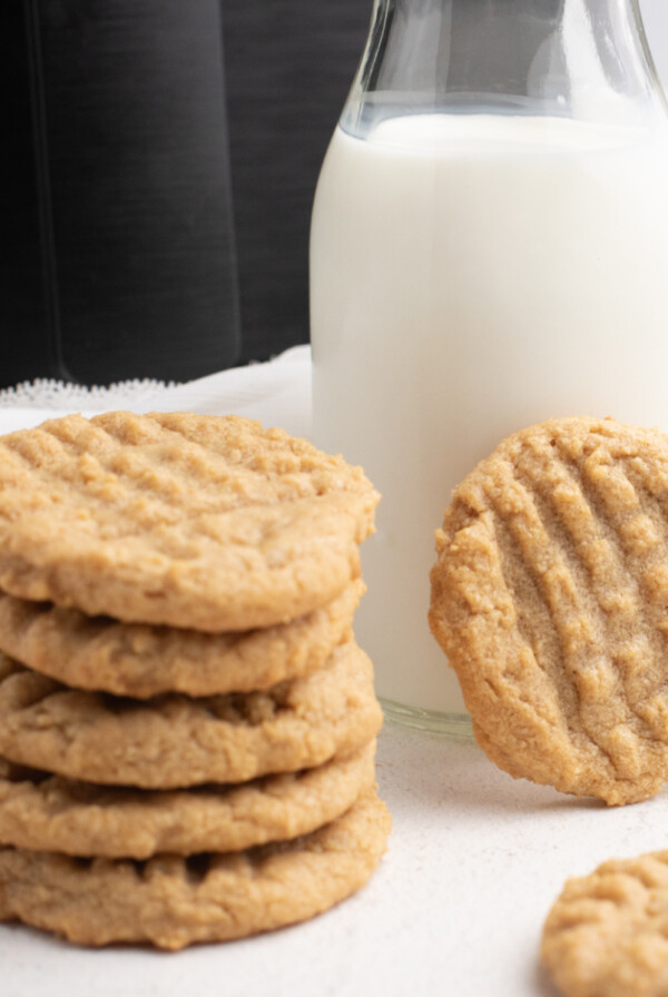 A stack of peanut butter cookies made in the Air Fryer with a glass of milk and the Air Fryer in the background.