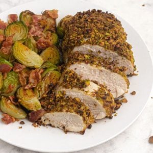 Cooked and sliced pistachio crusted chicken served with brussel sprouts on a white plate
