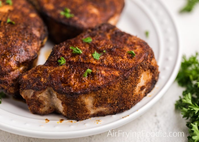 Thick cut pork chops on a white plate and topped with chopped parsley. 