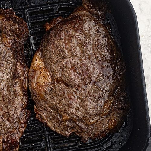 Juicy ribeye cooked steaks in the air fryer basket.