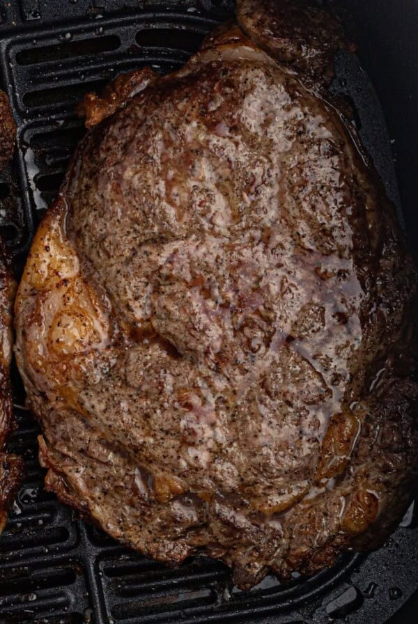 Juicy ribeye cooked steaks in the air fryer basket.