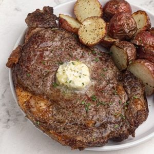 Juicy cooked air fryer ribeye steak served on a white plate, topped with melting butter.