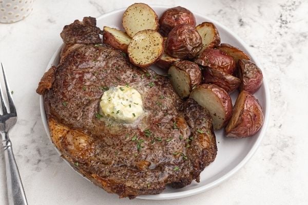 Juicy air fryer ribeye steak, served on a white plate with potatoes. 