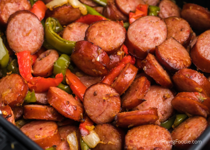 Close up photo of sausage and peppers in an air fryer basket. 