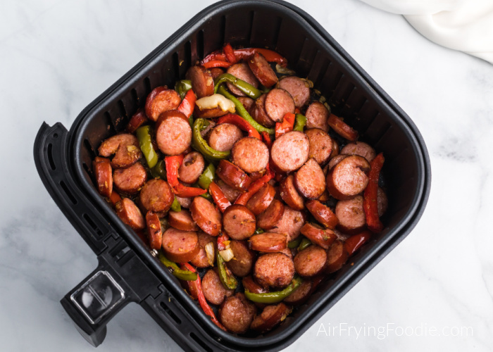 Cooked Sausage and peppers in an air fryer basket. 