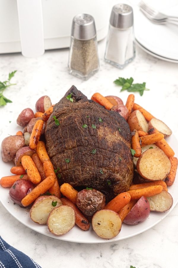 Juicy Top Round Roast served on a white plate, with potatoes, and carrots, seasoned with salt and pepper. 