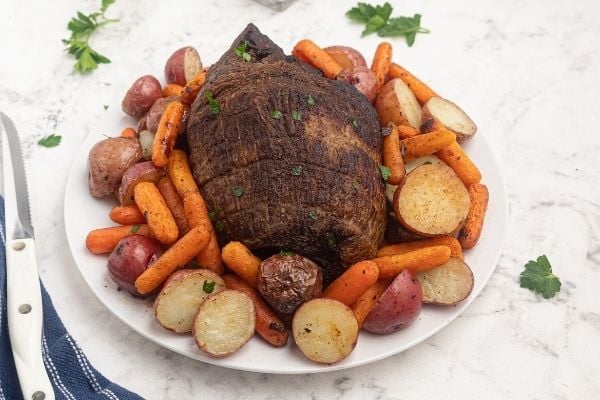 Air Fryer top round roast, cooked and served on a white plate with potatoes and carrots. 