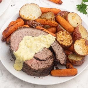 Air fryer top round roast, cooked and topped with bernaise sauce. Served with air fryer roasted potatoes and carrots.