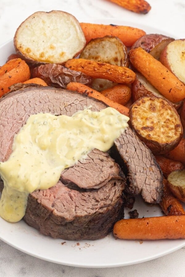 Air fryer top round roast, cooked and topped with bernaise sauce. Served with air fryer roasted potatoes and carrots.