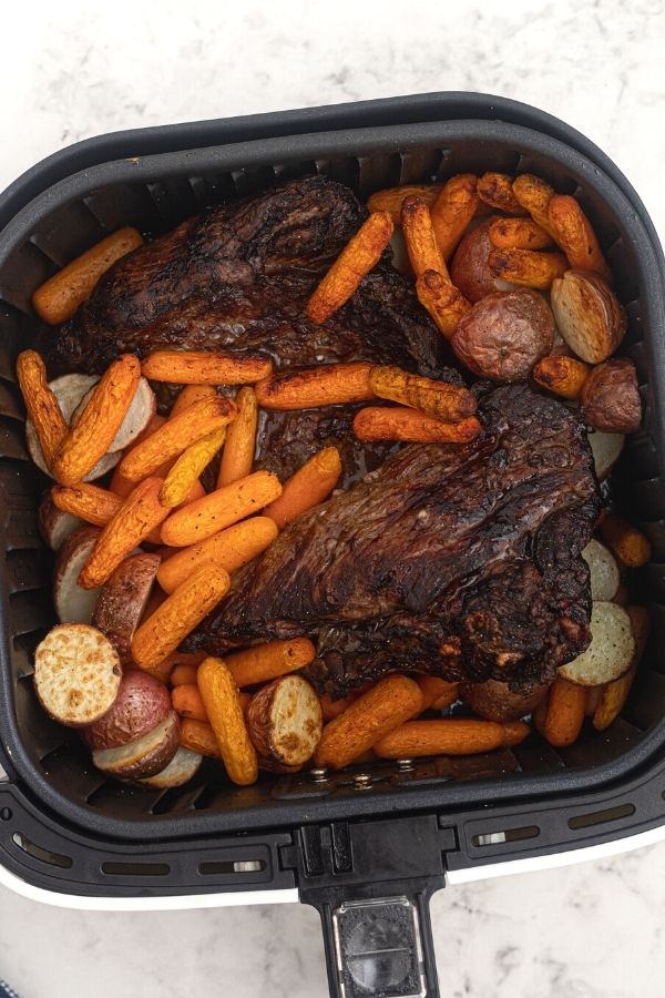 Roast, cooked in the air fryer basket, surrounded by potatoes and carrots. 