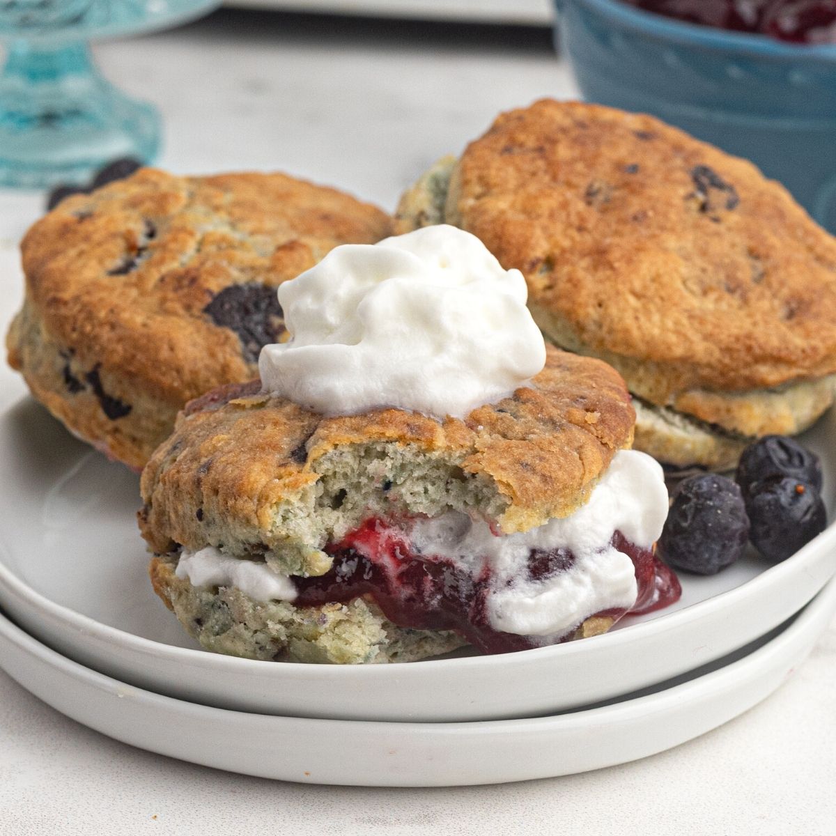 Air fryer blueberry scones, filled with jam and cream, served on a white plate.
