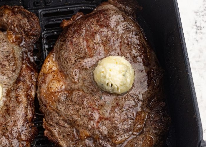 Juicy Air Fryer Ribeye steak, topped with butter, in an air fryer basket after being cooked. 