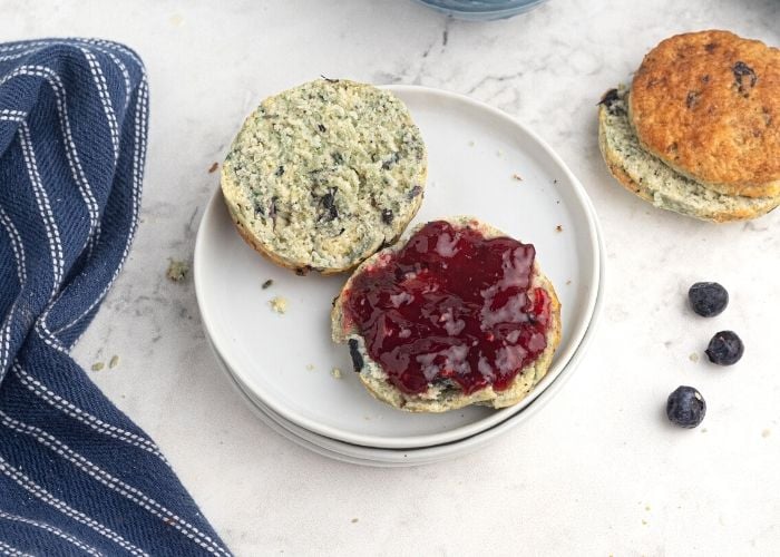 Blueberry scone, sliced in half and served with jam on a white plate. 