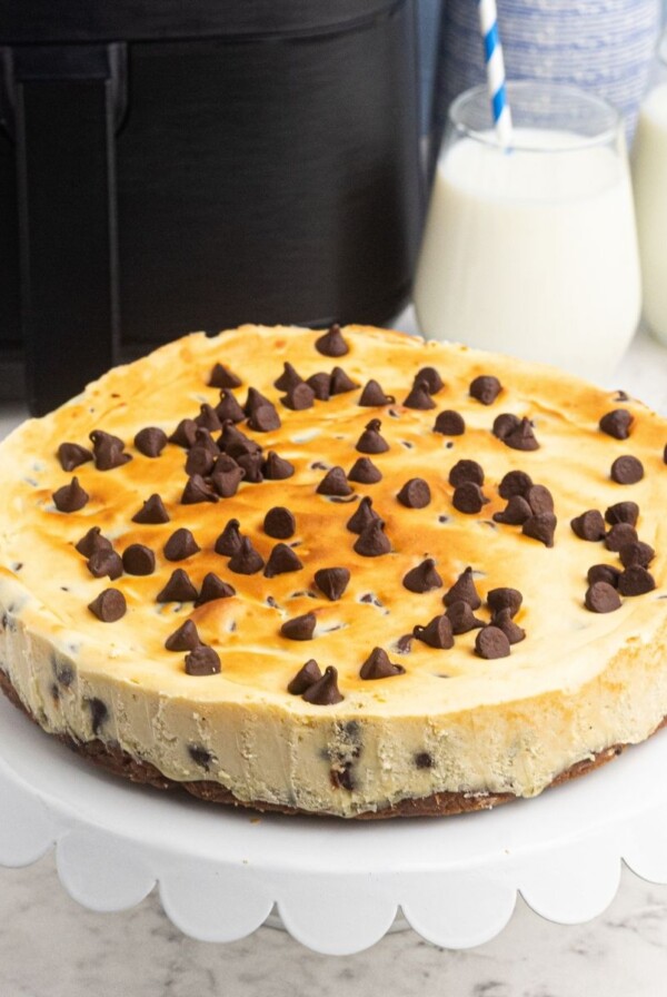 Air Fryer Chocolate Chip cheesecake on a white cake stand, in front of an air fryer.