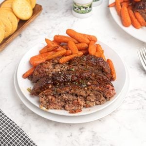 Cooked and sliced meatloaf on a white plate served with baby carrots.