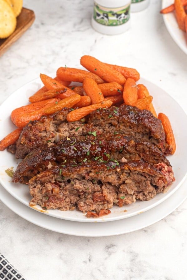 Cooked and sliced meatloaf on a white plate served with baby carrots.