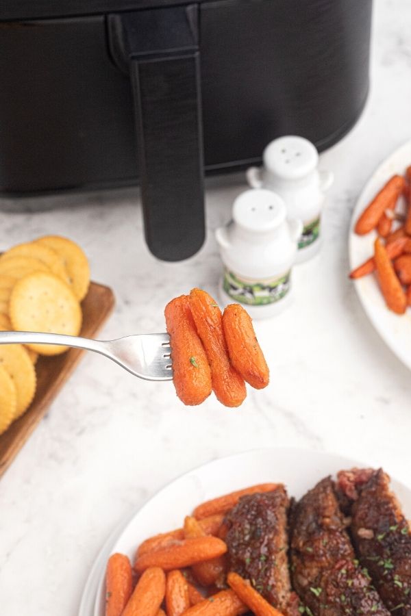 Air Fryer Honey Glazed Carrots on a fork, in front of the air fryer. 
