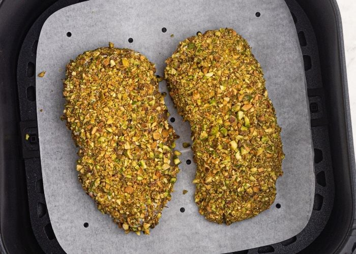 Pistachio Crusted chicken in the air fryer basket, before being cooked. 