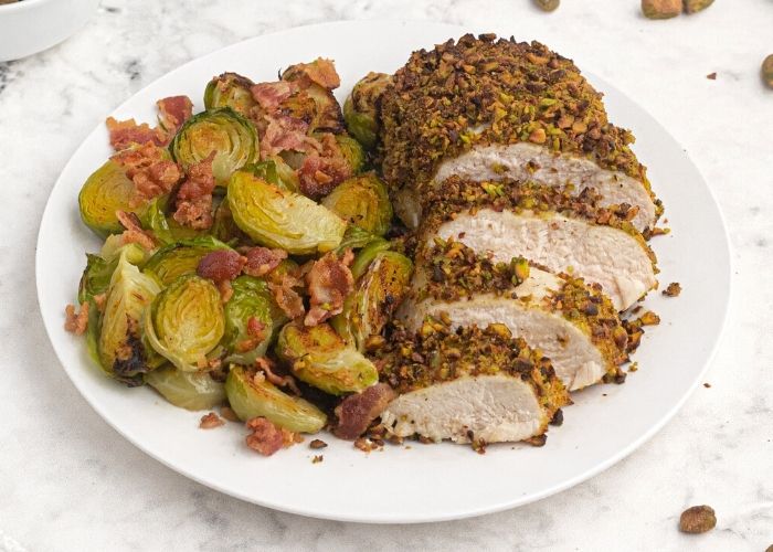 Pistachio crusted chicken on a white plate. sliced and served with brussel sprouts.