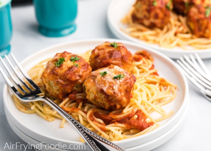 Air Fryer Chicken Parmesan meatballs  on a bed of spaghetti on a white plate. 