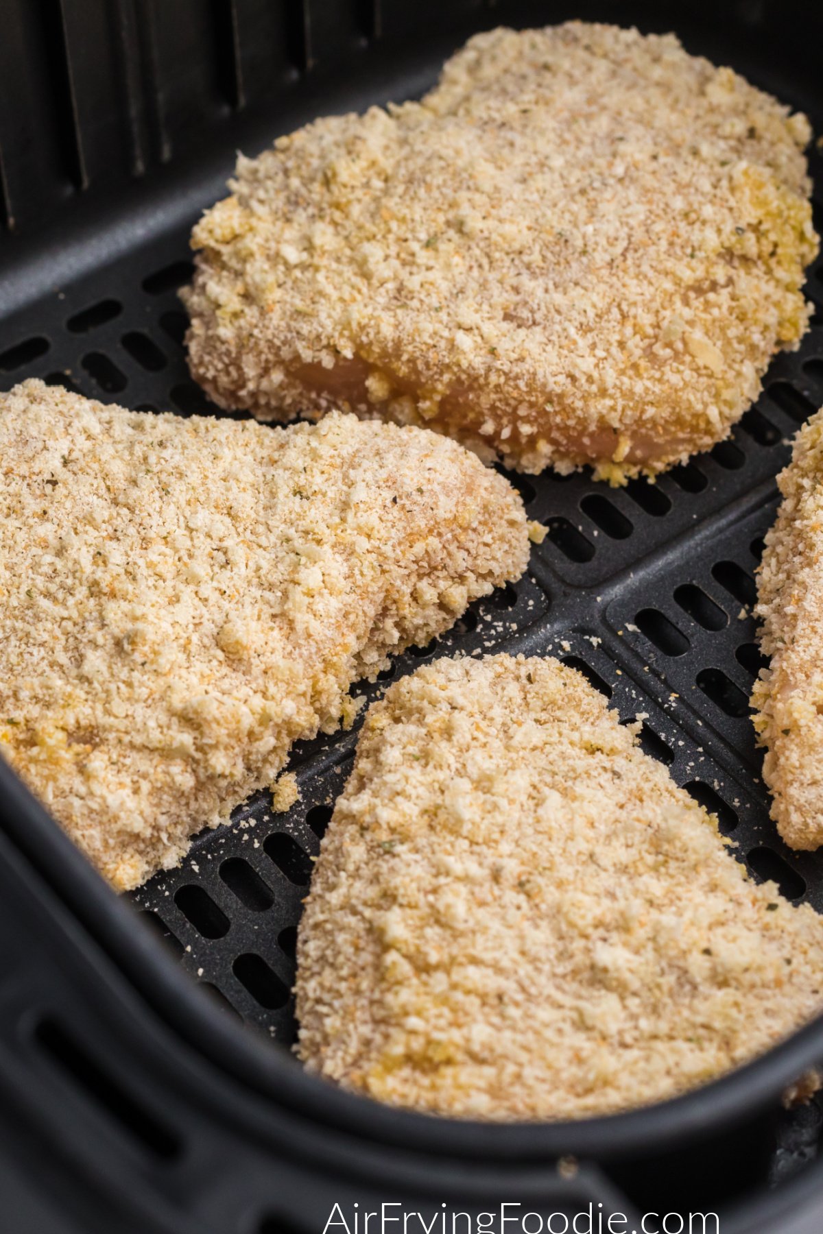 Coated parmesan chicken in the basket of the air fryer.
