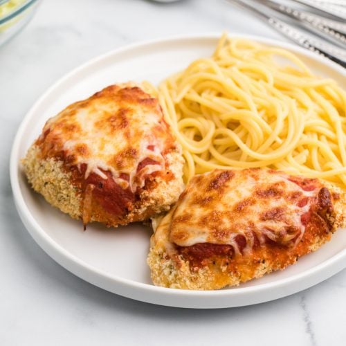 Air Fryer chicken parmesan on a white plate with spaghetti noodles.