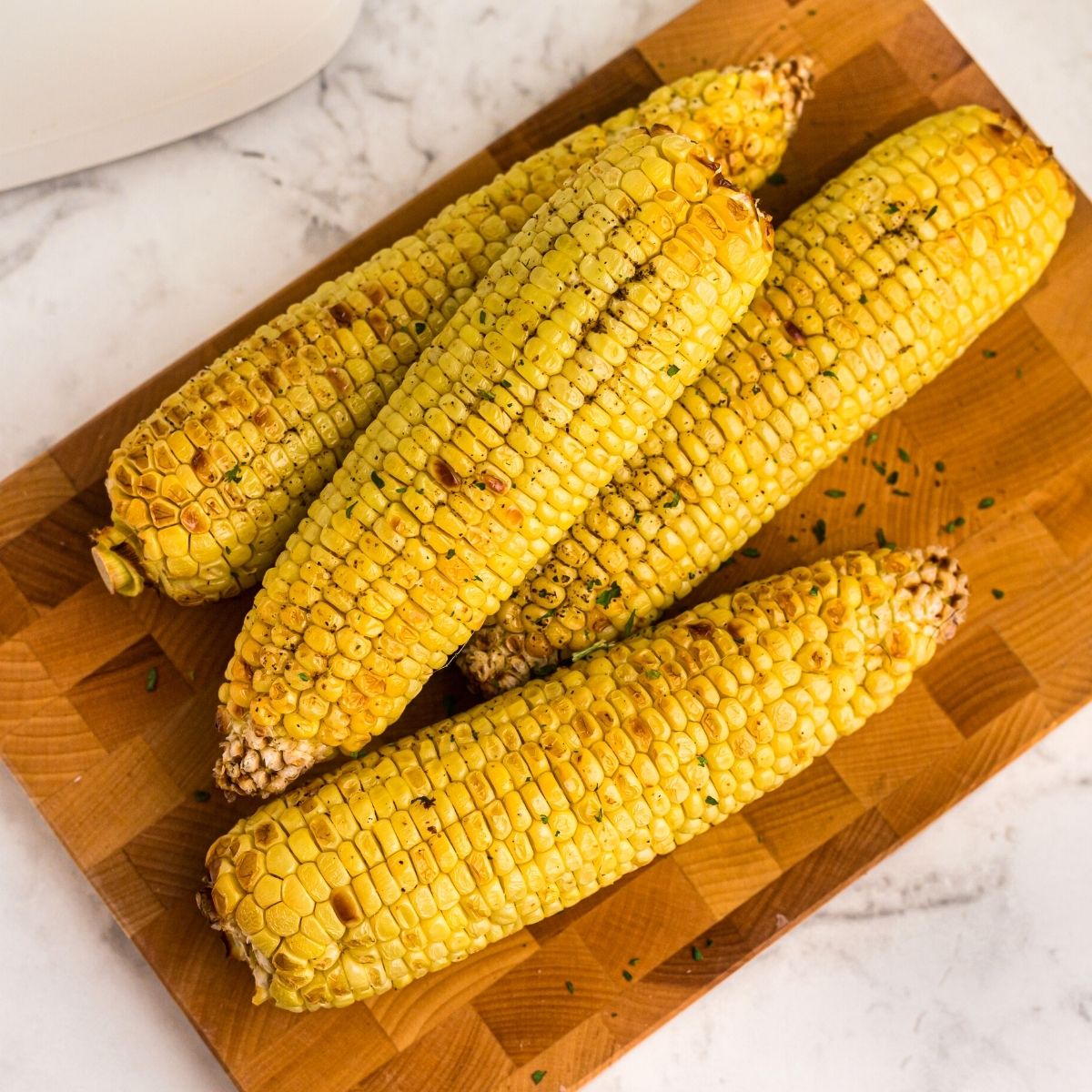Golden ears of corn on a board, buttered and seasoned.