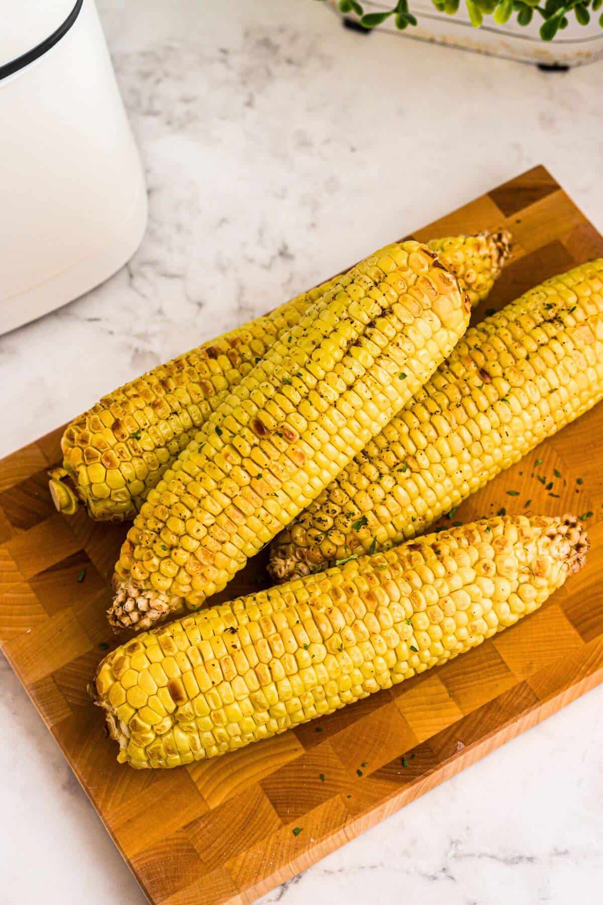 Golden yellow ears of corn on a wooden cutting board. 