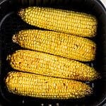 Golden yellow corn on the cob in the air fryer basket after being cooked and seasoned.