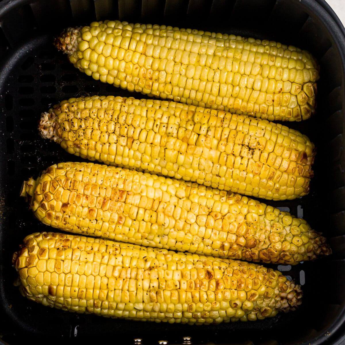 Golden yellow corn on the cob in the air fryer basket after being cooked and seasoned.