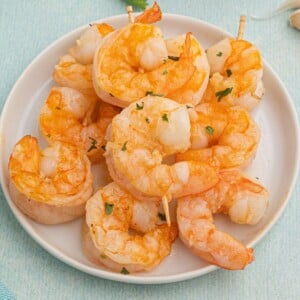 Golden orange shrimp, coated with butter and garlic, served on a white plate.