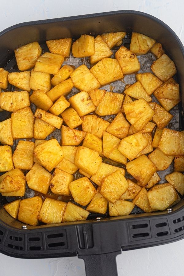 Juicy golden pineapple in the air fryer basket after being cooked in honey and bbq sauce. 