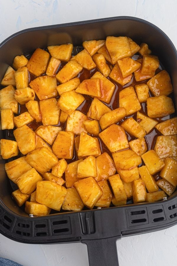 Juicy golden pineapple in the air fryer basket before being cooked in honey and bbq sauce.