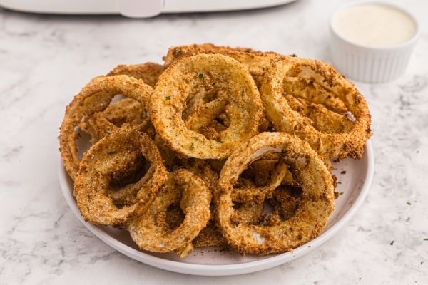 Golden crispy onion rings. Served on a white plate with ranch dressing on the side.