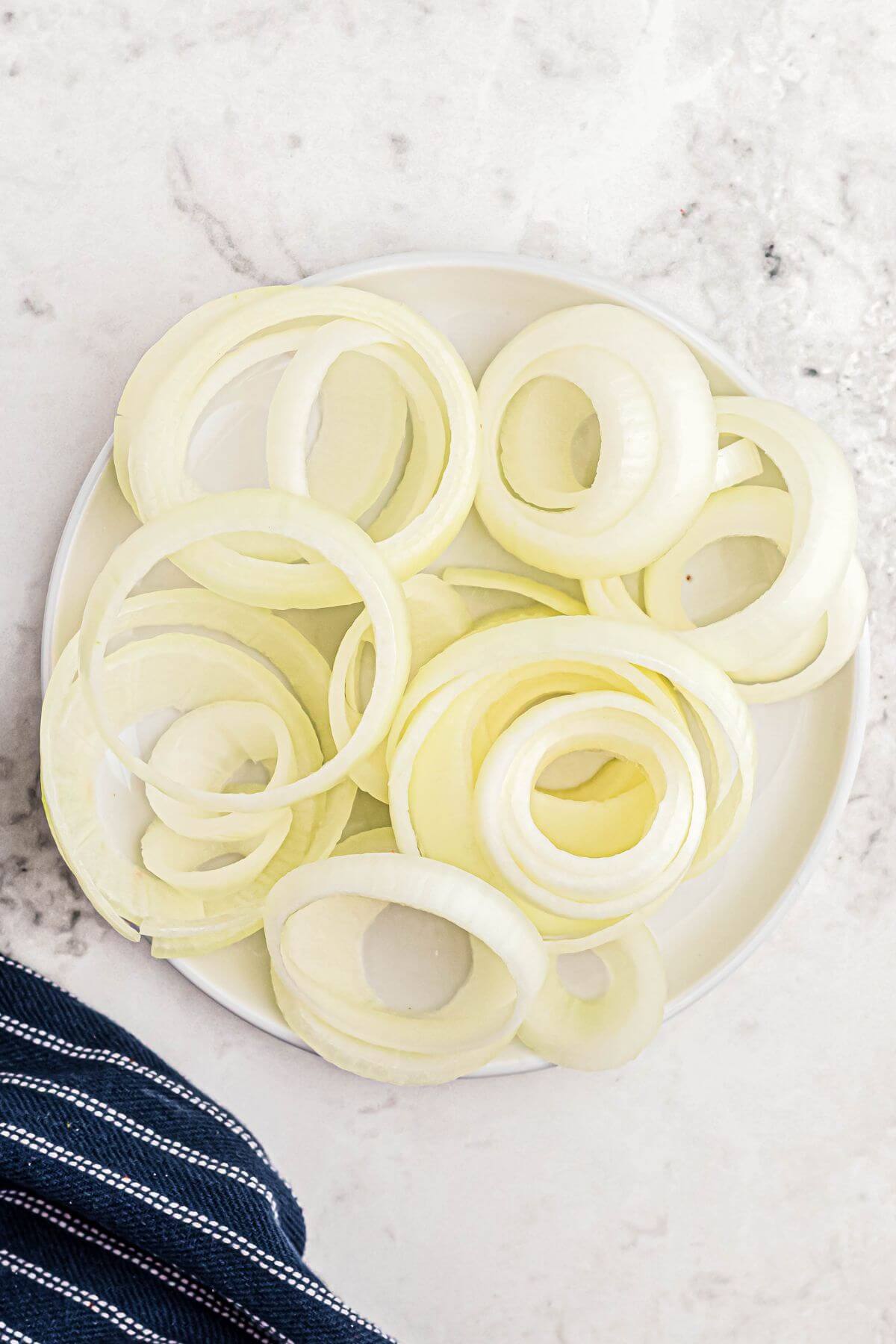 An onion sliced into rings, stacked on a white plate. 