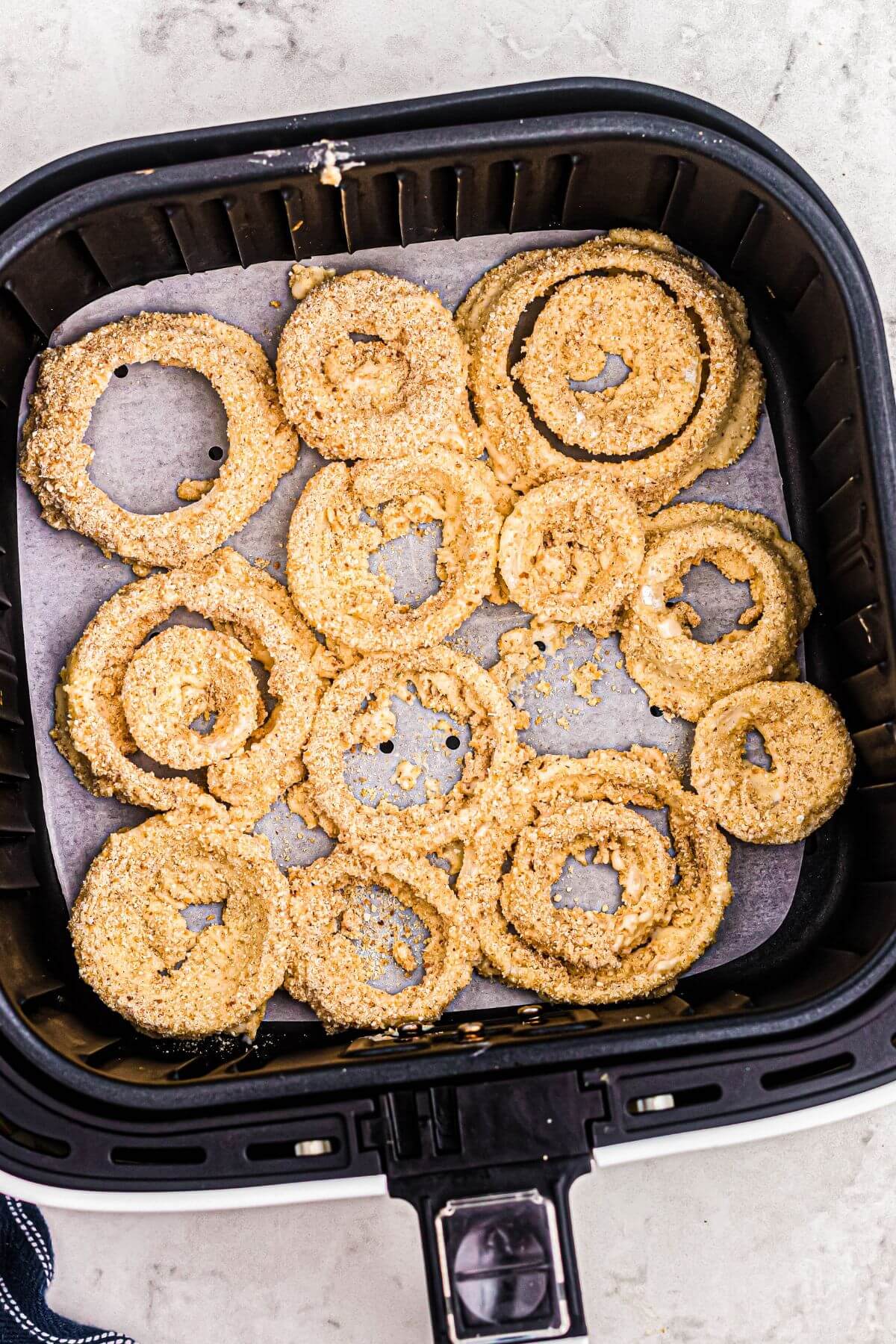 Uncooked battered onion rings in the air fryer basket, lined with parchment paper. 