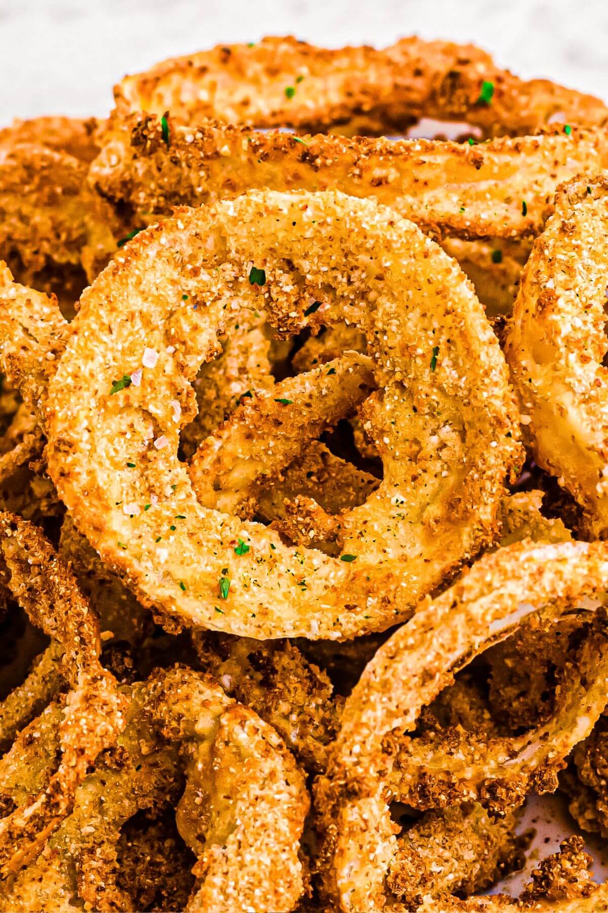 Golden crispy battered onion rings stacked on a white plate.